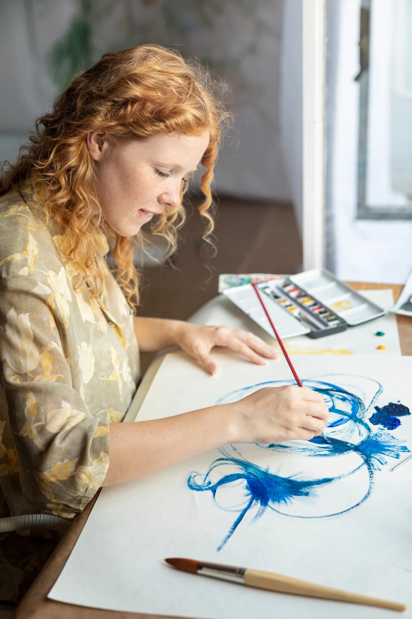 Mulher ruiva pintando traços azuis de aquarela em uma folha