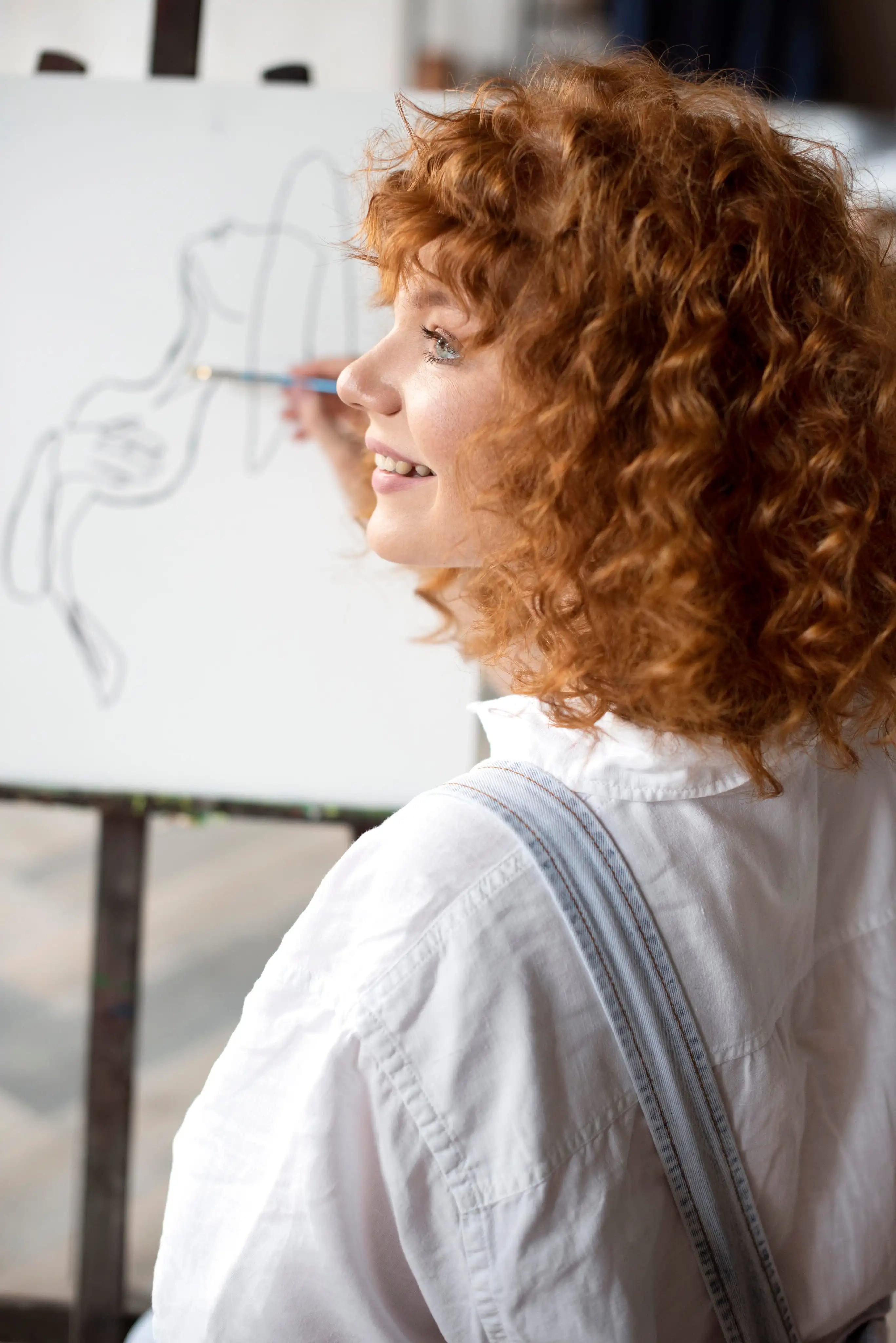 Mulher ruiva sorridente desenhando uma figura em um cavalete