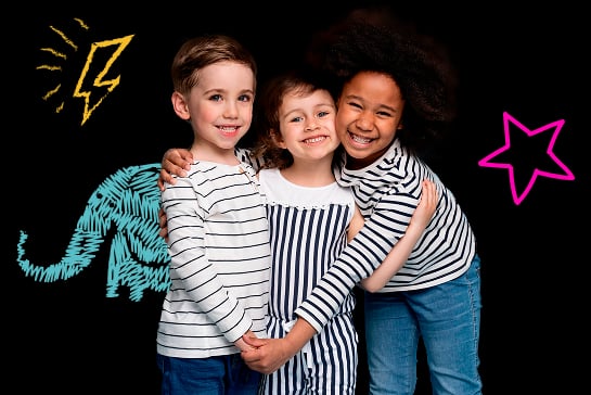 Três crianças sorrindo abraçadas com ilustrações coloridas de um elefante, um raio e uma estrela ao fundo