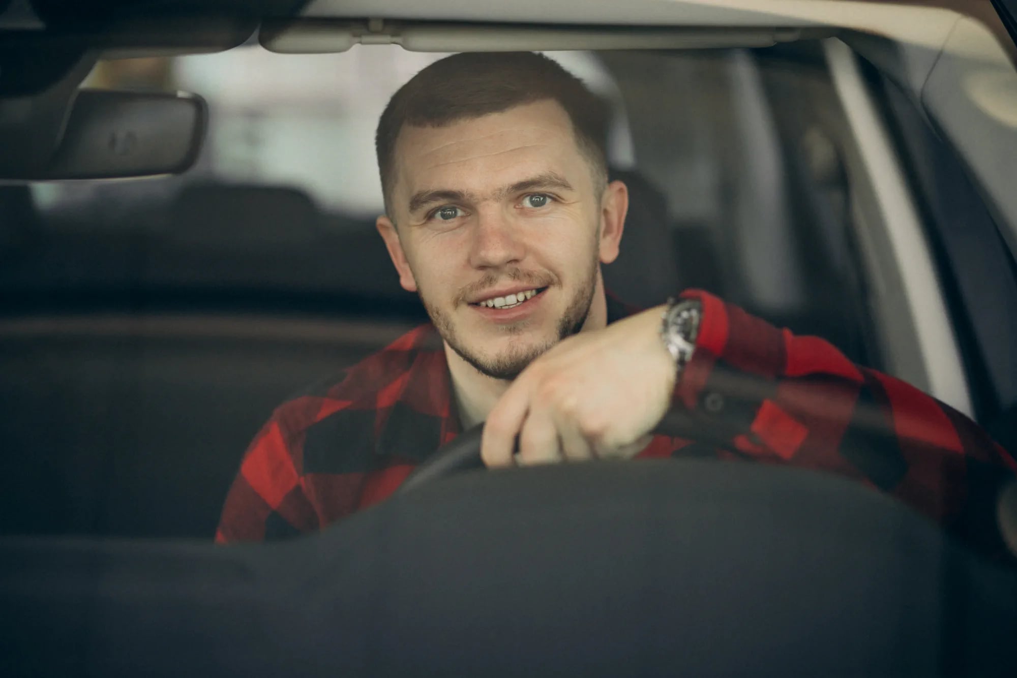 Homem sorridente ao volante de um carro, com o braço apoiado na direção